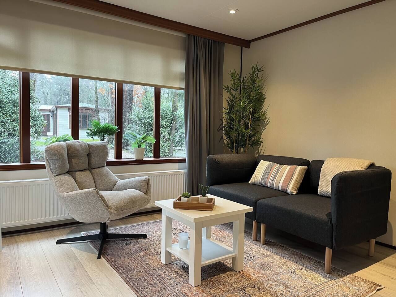 Un salon moderne avec un fauteuil gris, un canapé noir et une table basse blanche.