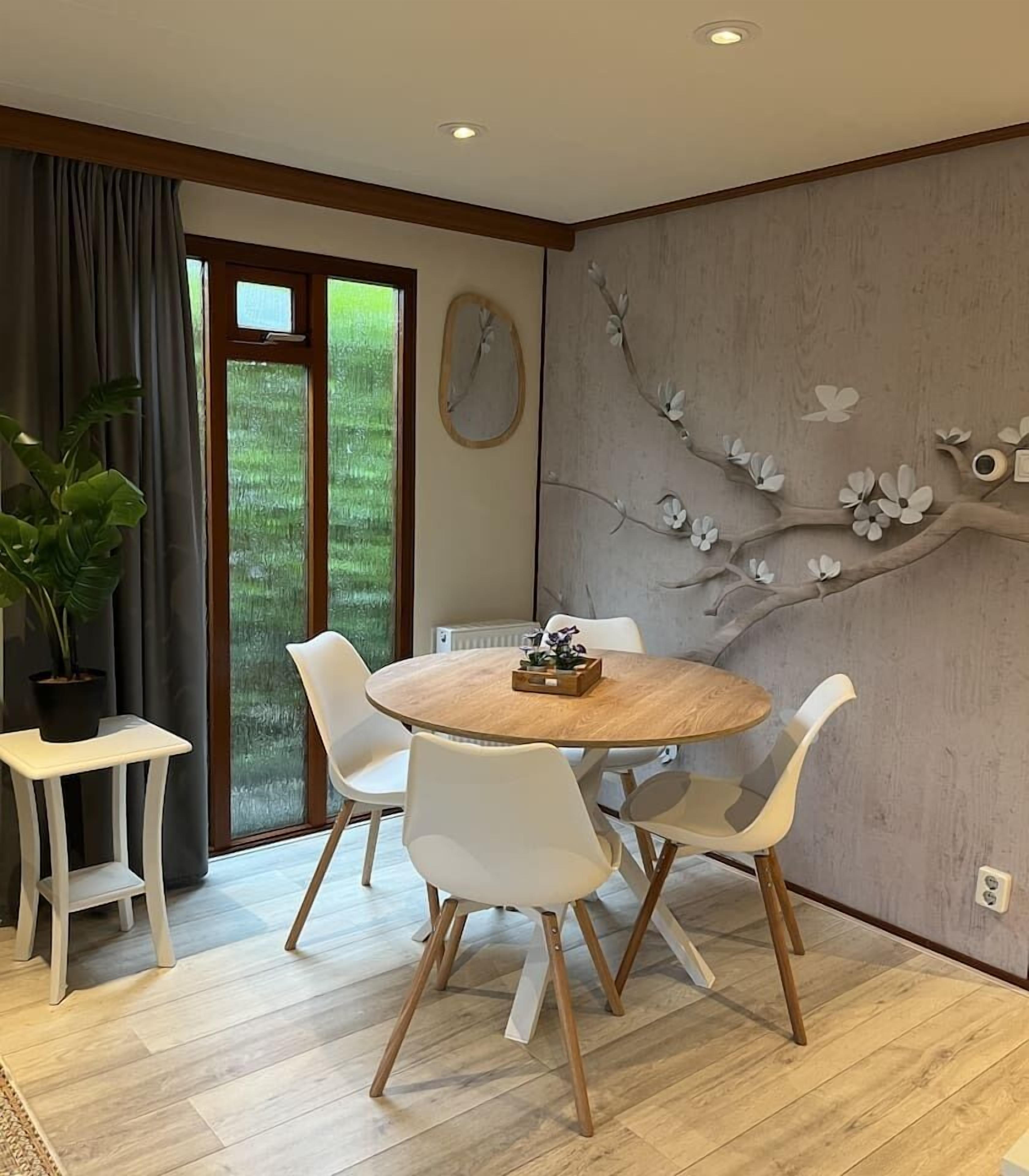 Un coin repas avec une table ronde en bois, des chaises blanches et une plante en pot.