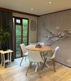 Un coin repas avec une table ronde en bois, des chaises blanches et une plante en pot.