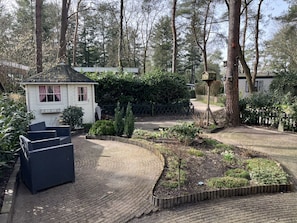 Un espace jardin agrémenté d’un petit bâtiment blanc, de meubles en osier et d’un chemin pavé.