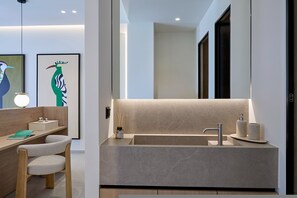 A modern bathroom with a large mirror, a sink, and a toilet. There is a wooden vanity with a chair and a framed picture on the wall.