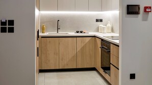 A modern kitchen with wooden cabinets, a sink, and a countertop. There are recessed ceiling lights and a small digital display on the wall. - Executive Apartment by Fasma Suites (Pireas)