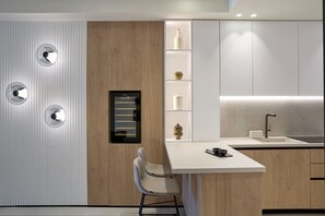 A modern kitchen with a wooden accent wall, built-in shelves, a white countertop, and a single chair.