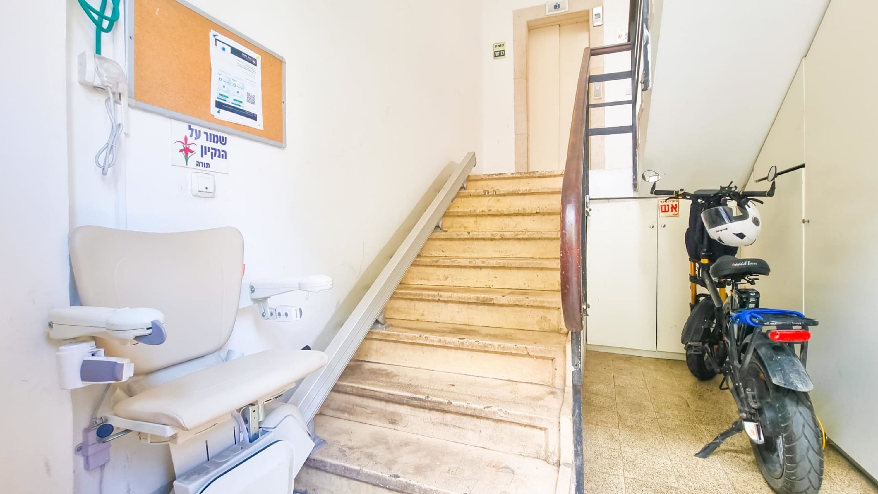 Un escalier menant à une porte, un fauteuil roulant et une moto dans un couloir.