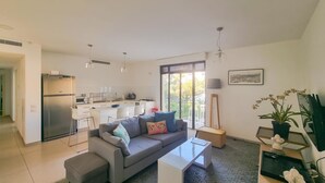 A modern living room with a grey sofa, a coffee table, and a kitchen in the background. - Nitsana Cachemire in Tel Aviv-Yafo (Tel Aviv-Yafo)