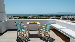 A terrace with two chairs and a table, overlooking a coastal landscape with buildings and mountains. - Naxos Kastraki Homey Villa with Sea View (Kastraki)