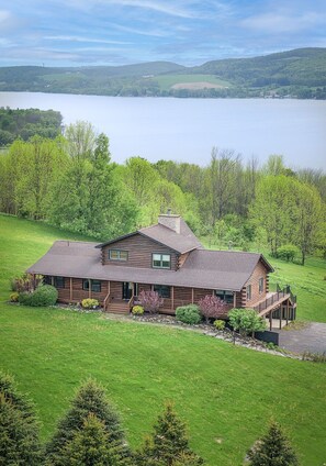 Une cabane en rondins dotée d’un porche, entourée d’un paysage verdoyant luxuriant et avec un lac en arrière-plan.