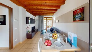 Eine moderne Küche mit Holzbalken, einem Essbereich mit Tisch für vier Personen und einem Wohnbereich mit Sofa und Kunstwerk an der Wand.