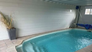 Una piscina rectangular techada con piso y paredes de azulejos, una planta en maceta y un ventanal.