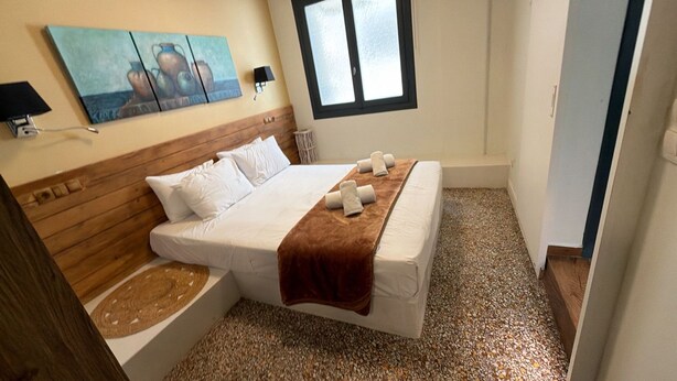 A bedroom with a bed, a headboard, a painting, a window, and a small bathroom. - Athenian Stay 301 By VPN (Athens)