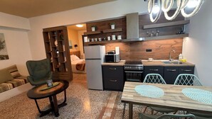 A compact living space with a kitchenette, a dining area with a table and chairs, a sofa, a small side table, and a bookshelf. - Athenian Stay 301 By VPN (Athens)