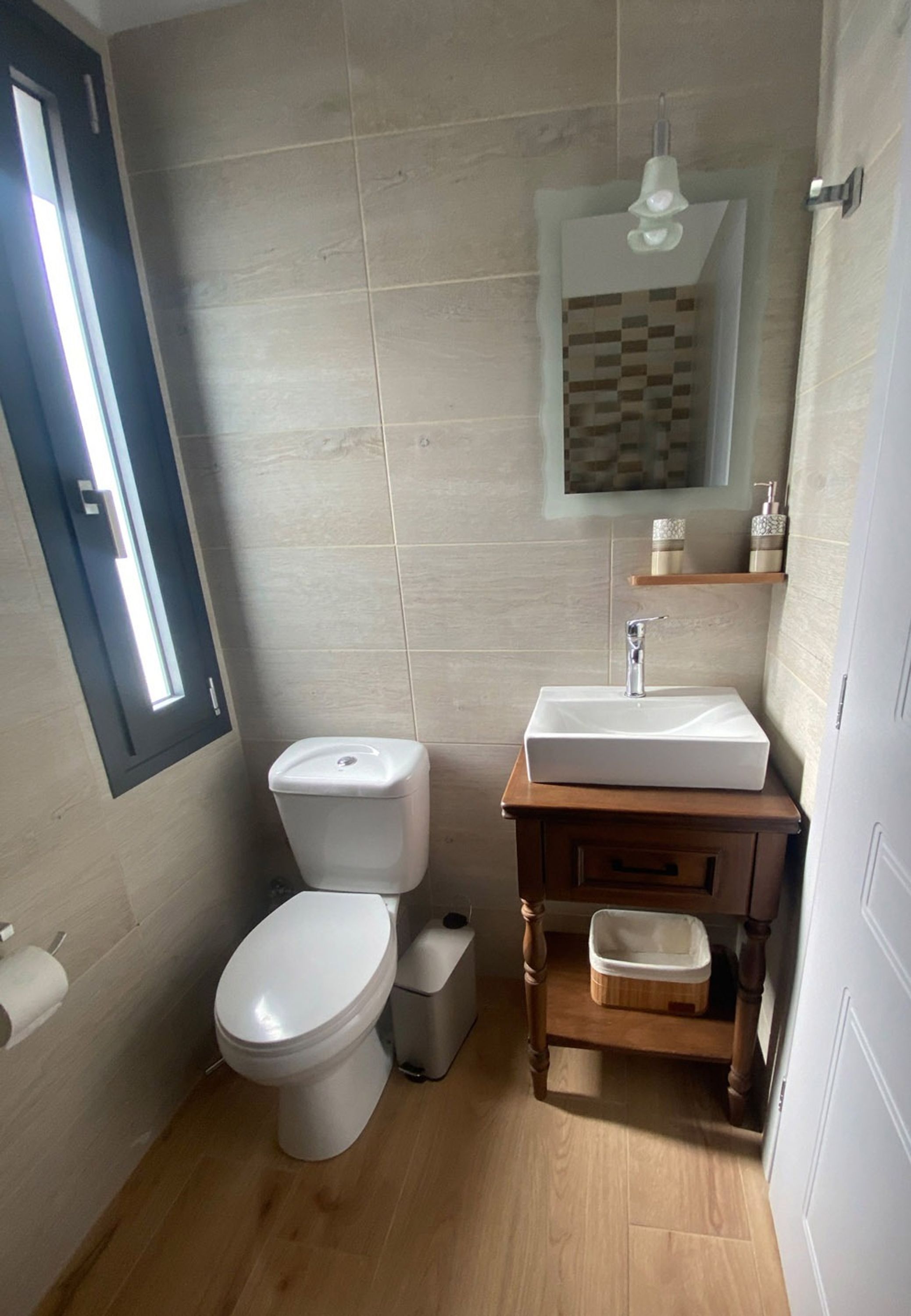 A bathroom with a toilet, sink, mirror, and wooden cabinet.