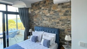 Una camera da letto con parete in pietra, un letto grande con lenzuola blu, due comodini con lampade e un condizionatore d'aria.