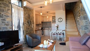 Un soggiorno accogliente con TV, divano, tavolo da pranzo con candele e una scala che conduce a una cucina con pareti in pietra.