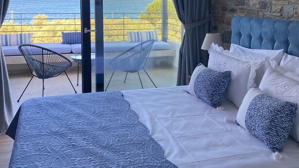 Una camera da letto con un letto grande, vista mare e un muro in pietra.
