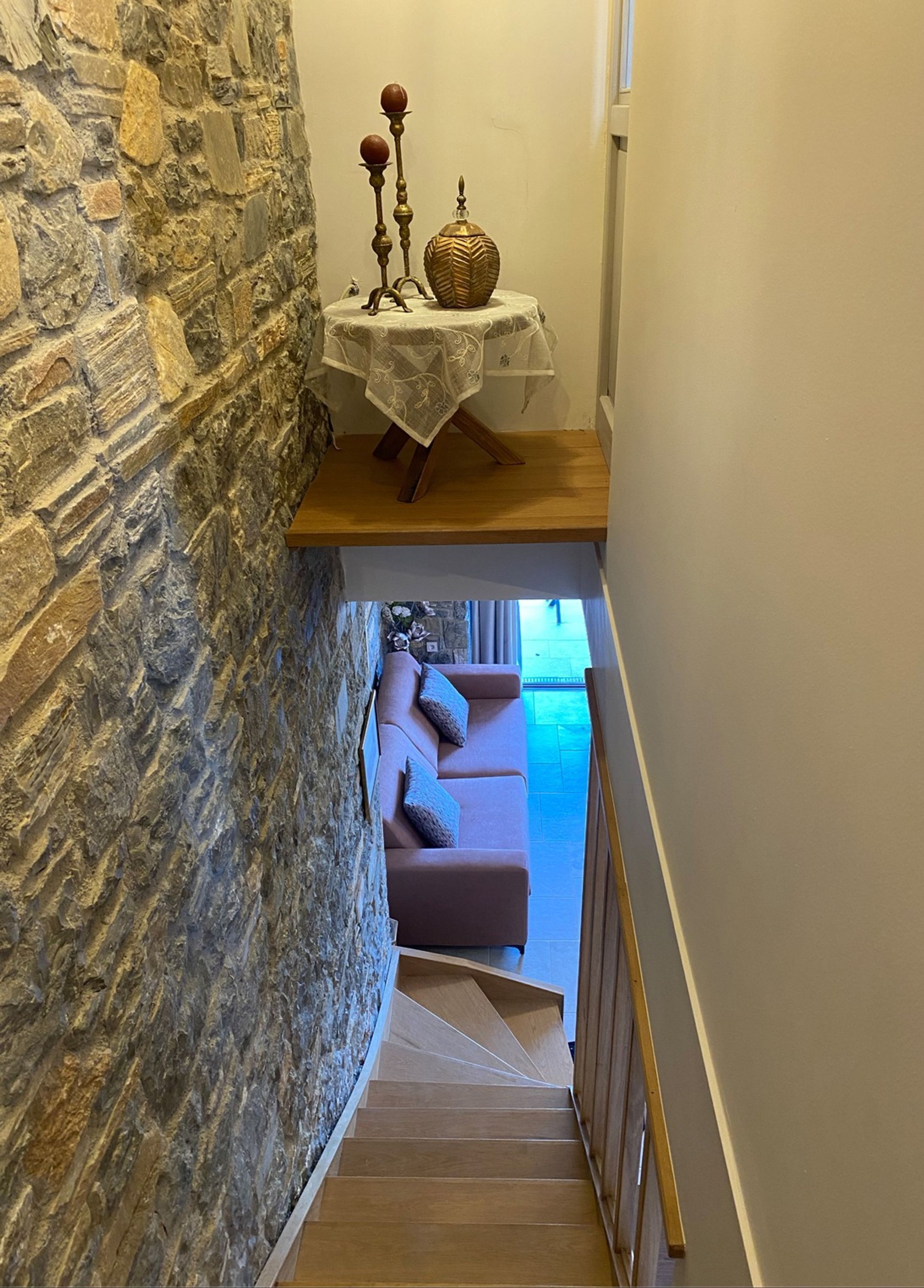 A staircase leading to a living area with a stone wall, a table with a decorative vase, and a sofa.