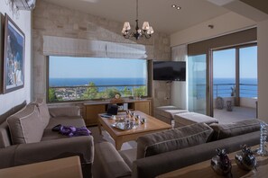 Een moderne woonkamer met een groot raam, een flatscreen-televisie en een balkon met uitzicht op zee.