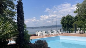 A swimming pool with white lounge chairs and a view of the sea. - Sirmio Green Shore By Bookinggardalake (Sirmione)