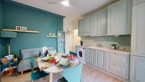 A modern kitchen with teal walls, a dining area with a table set for two, and light-colored cabinets. - Sirmio Green Shore By Bookinggardalake (Sirmione)