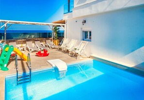 A pool area with lounge chairs, a slide, and a ladder. - Thalassa Beachfront Villa with private pool (Prinos)