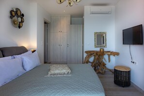 A bedroom with a bed, a wooden headboard, a wall-mounted TV, a mirror, and a wardrobe. - Thalassa Beachfront Villa with private pool (Prinos)