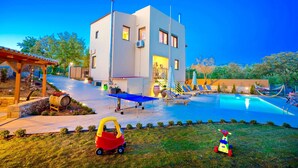 Una casa moderna de dos pisos con piscina, mobiliario de exterior y una pérgola.