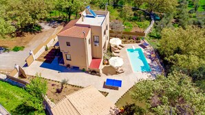 Un edificio de dos pisos con piscina, mobiliario exterior y cancha de tenis.