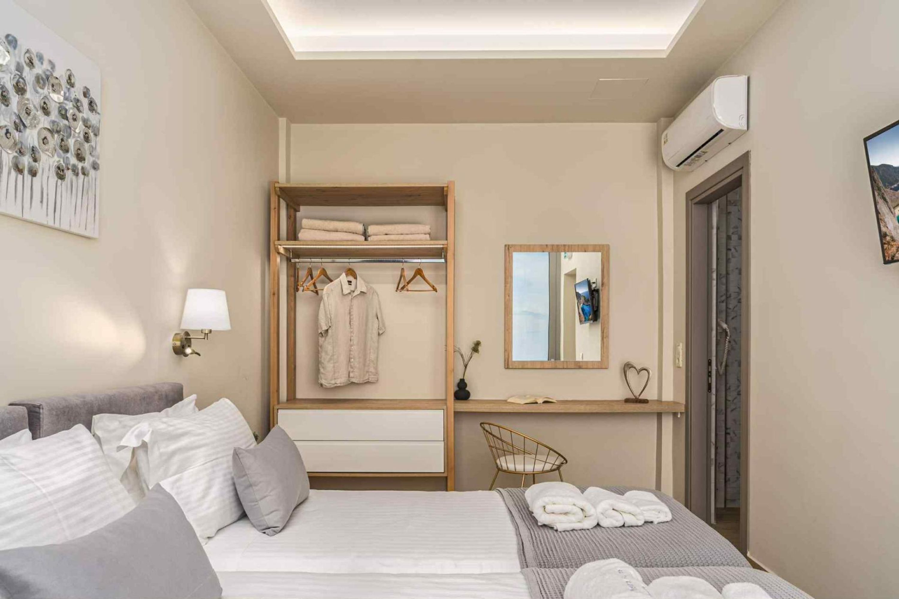 Quarto de hotel com cama, guarda-roupa, espelho, pequena mesa com luminária e ar condicionado.