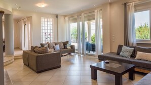 A spacious living room with a sofa set, a coffee table, and a view of the outdoors through large windows. - Villa Rafaella in Rethymno (Rethymno)