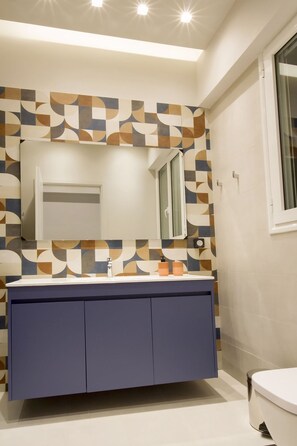 A bathroom with a geometric patterned wall, a mirror, a white sink, and a blue cabinet. - Acropolis Luxury retreat (Athens)