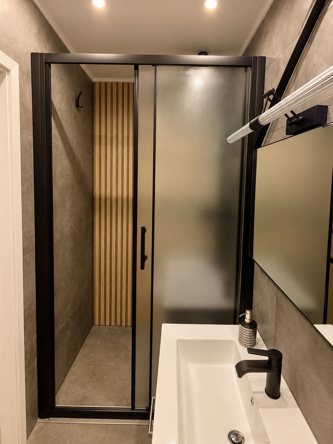 A modern bathroom with a walk-in shower, a large mirror, and a white sink.