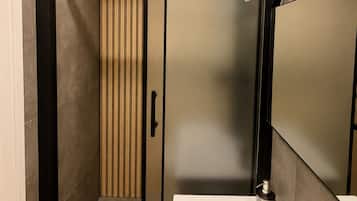 A modern bathroom with a walk-in shower, a large mirror, and a white sink.