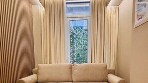 A modern living room with a beige sofa, wooden paneling on one wall, and a window with curtains. - Monastiraki 110 @SuperHost Hub (Athens)