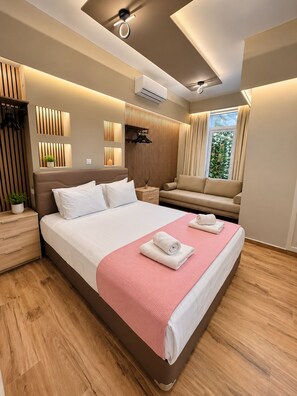 A modern hotel room with a large bed, a sofa, a small table, and a window with curtains. - Monastiraki 110 @SuperHost Hub (Athens)