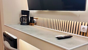 A modern kitchenette with a built-in TV, a coffee maker, and a remote control on the counter. - Monastiraki 110 @SuperHost Hub (Athens)