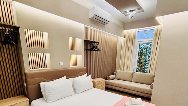 A modern hotel room with a large bed, a sofa, a wooden wardrobe, and a ceiling fan. - Monastiraki 110 @SuperHost Hub (Athens)