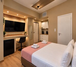 Una habitación de hotel con cama, escritorio, silla, televisión y kitchenette.