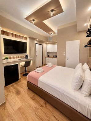 A modern hotel room with a large bed, a flat-screen TV, a desk with a chair, a kitchenette, and a ceiling fan. - Monastiraki 110 @SuperHost Hub (Athens)