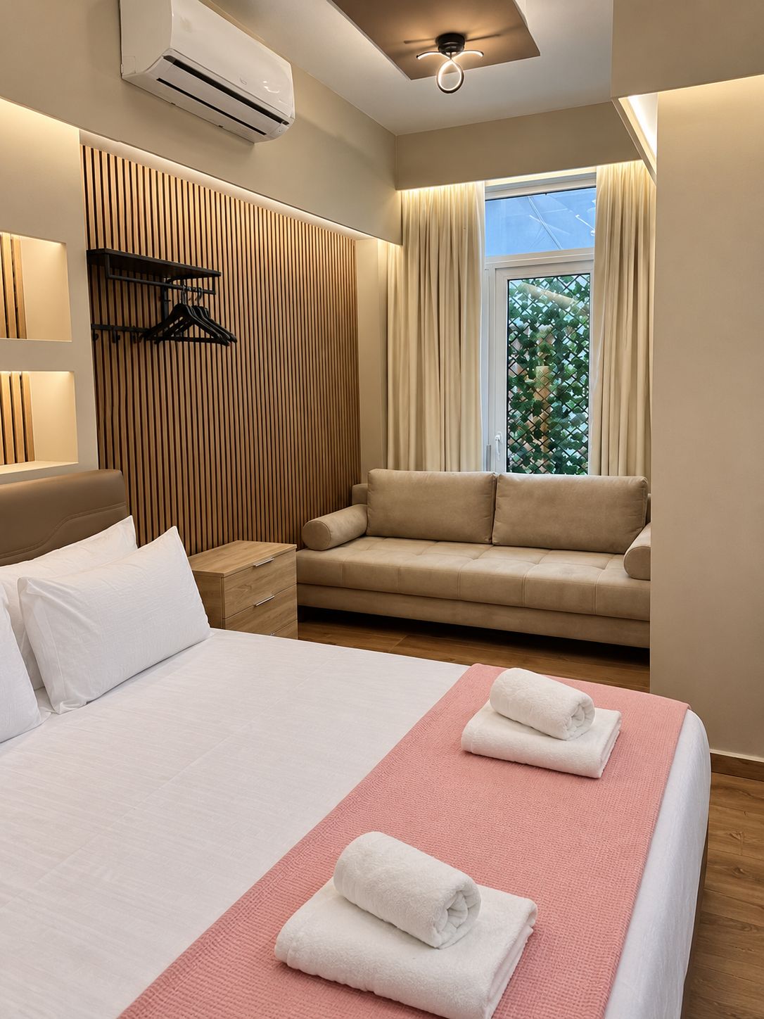 A hotel room with a bed, a sofa, a bedside table, a wardrobe, and a window with curtains.