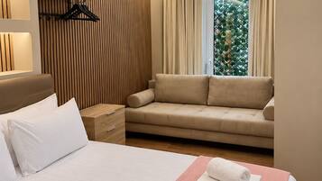 A hotel room with a bed, a sofa, a bedside table, a wardrobe, and a window with curtains.