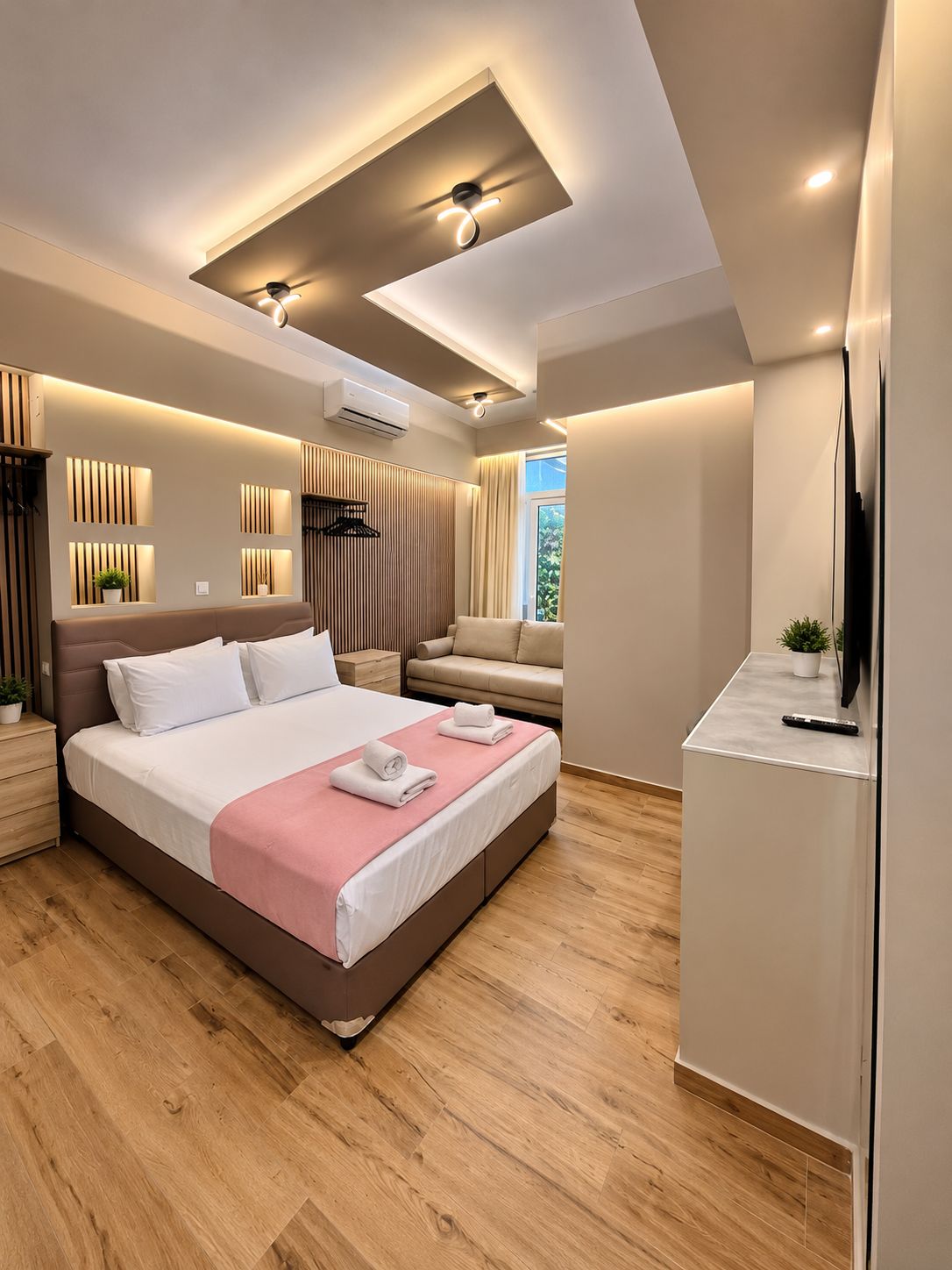 A modern bedroom with a large bed, bedside tables, a sofa, and a TV.
