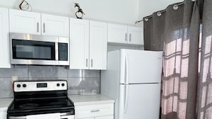 A compact kitchen with white cabinets, a microwave, a stove, and a refrigerator. - 2-bedrooms next to Grace Bay (Grace Bay)