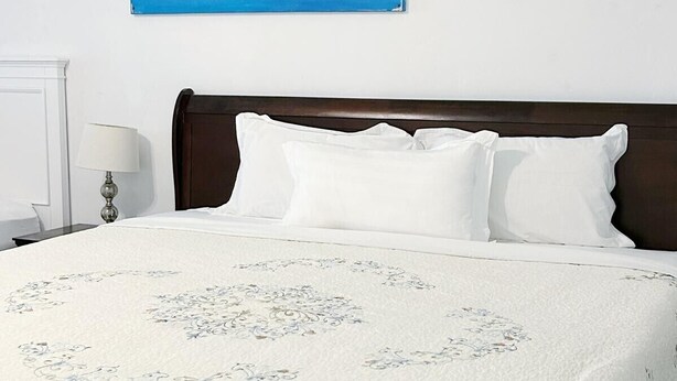 A neatly made bed with a white bedspread and pillows, a dark wooden headboard, and a wall-mounted painting of a blue seascape. - 2-bedrooms next to Grace Bay (Grace Bay)