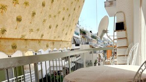 A balcony with a patterned canopy, white metal railings, a table with a patterned tablecloth, and a chair with a palm leaf design. - Modern Apartment in Athens Center (Athina)