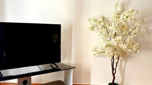 A flat-screen TV on a glass TV stand in a room with wooden flooring and a white wall. - Modern Apartment in Athens Center (Athina)