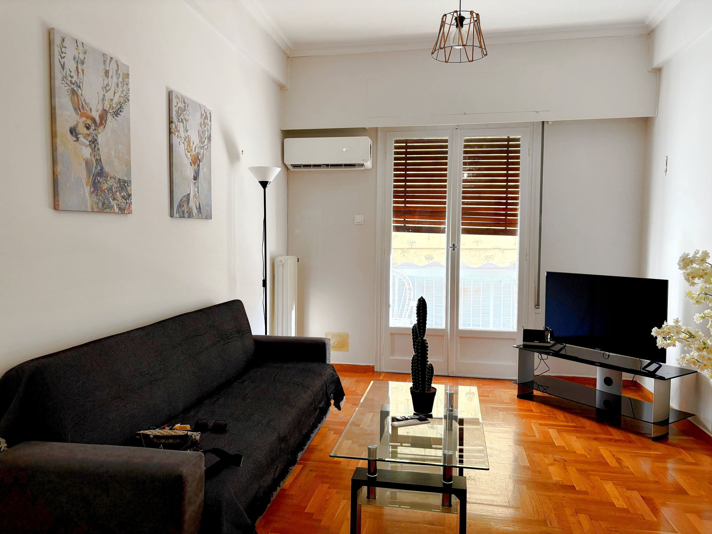A living room with a black sofa, a glass coffee table, a TV, and artwork on the wall.