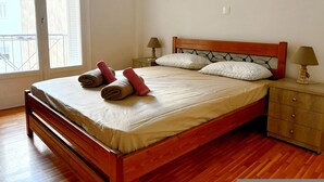 A neatly made bed with rolled towels, a wooden headboard, two bedside tables with lamps, and a view of the outside through a window. - Modern Apartment in Athens Center (Athina)