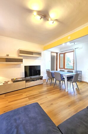 Uma sala de estar moderna com televisão de tela plana, mesa de jantar e cadeiras.