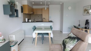 Eine moderne Küche mit Essbereich, einem Sofa mit Palmenblattkissen und einem kleinen Tisch mit Lampe.