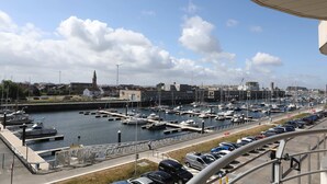 Ein Yachthafen mit vertäuten Booten, eine Straße mit Autos und Gebäude im Hintergrund.